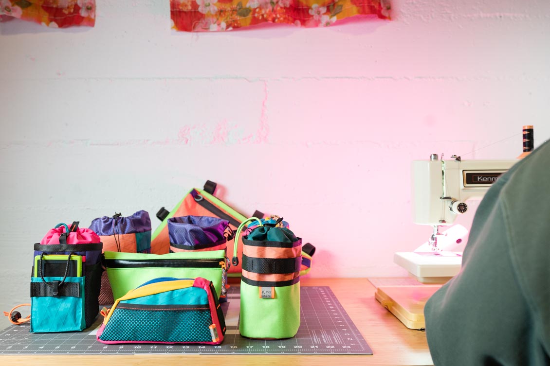 A bunch of bags on a sewing table, next to the seamstress.